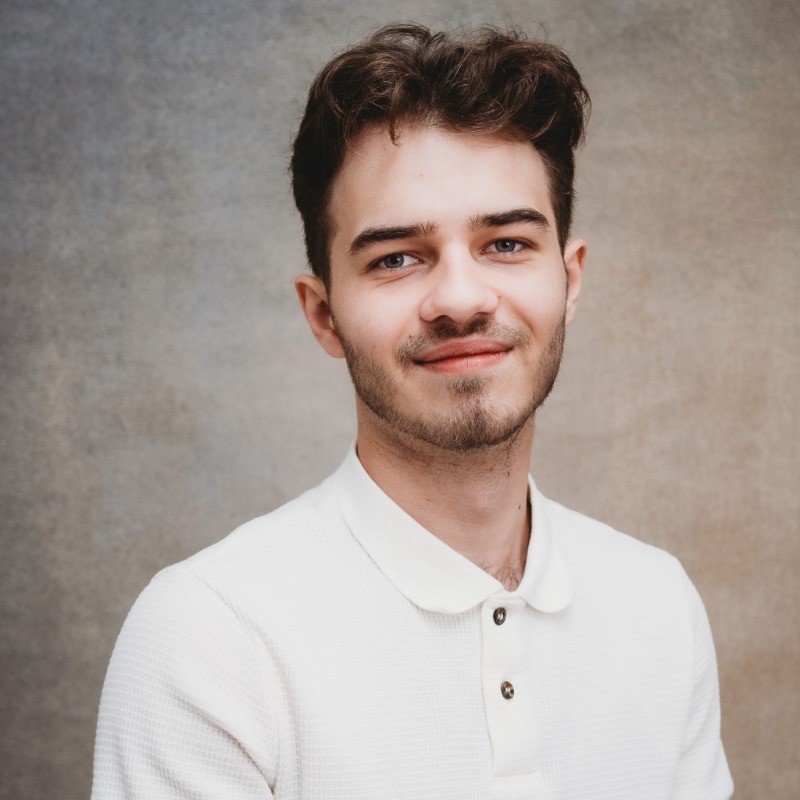 Headshot of man in a white button shirt with a brown background.